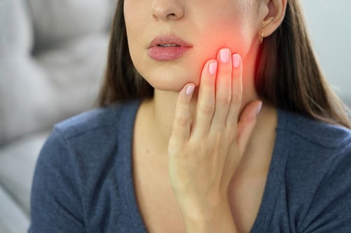 Woman holding the side of her jaw while experiencing tooth or jaw pain.