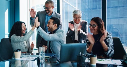 A group of colleagues celebrating a workplace achievement with high-fives and applause, highlighting the importance of recognising milestones, shared success and positive encouragemen