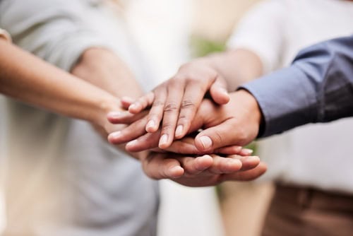 Close-up of a diverse group of people stacking their hands together, representing peer accountability, teamwork, encouragement and mutual support in achieving personal goals.